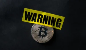 Bitcoin coin covered with yellow warning tape symbolizing awareness of Common Crypto Scams in 2025.