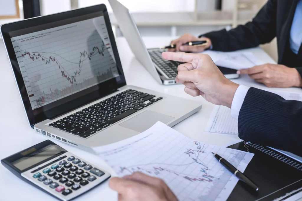Business professionals analyzing corporate bond charts on laptops and financial reports during a market performance review meeting in 2025.