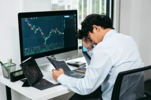 Trader feeling stressed while reviewing forex charts on computer and tablet, illustrating emotional pressure behind why traders fail in 2025.