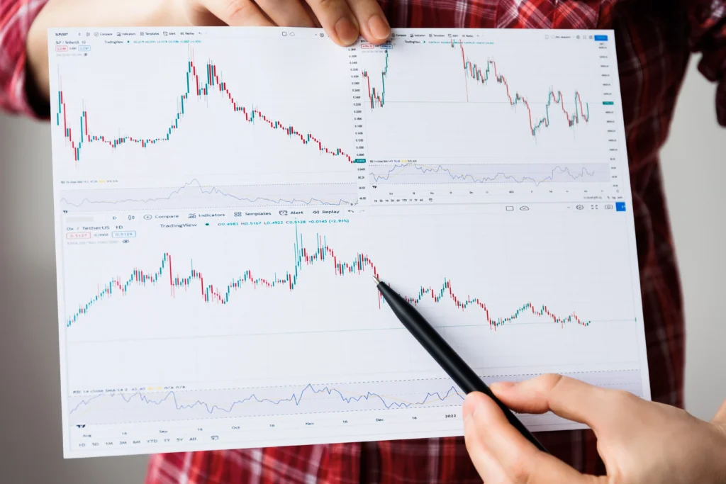 Person holding multiple trading charts and pointing at market trends with a pen.
