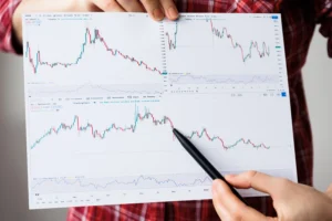 Person holding multiple trading charts and pointing at market trends with a pen.