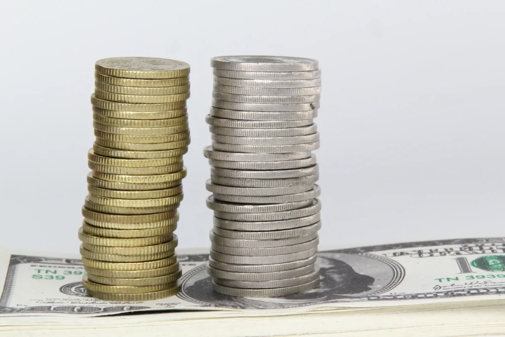 Stacks of gold and silver coins placed on US dollar notes representing the Silver vs Gold investment comparison in 2025.