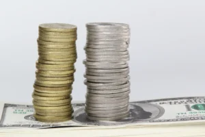 Stacks of gold and silver coins placed on US dollar notes representing the Silver vs Gold investment comparison in 2025.