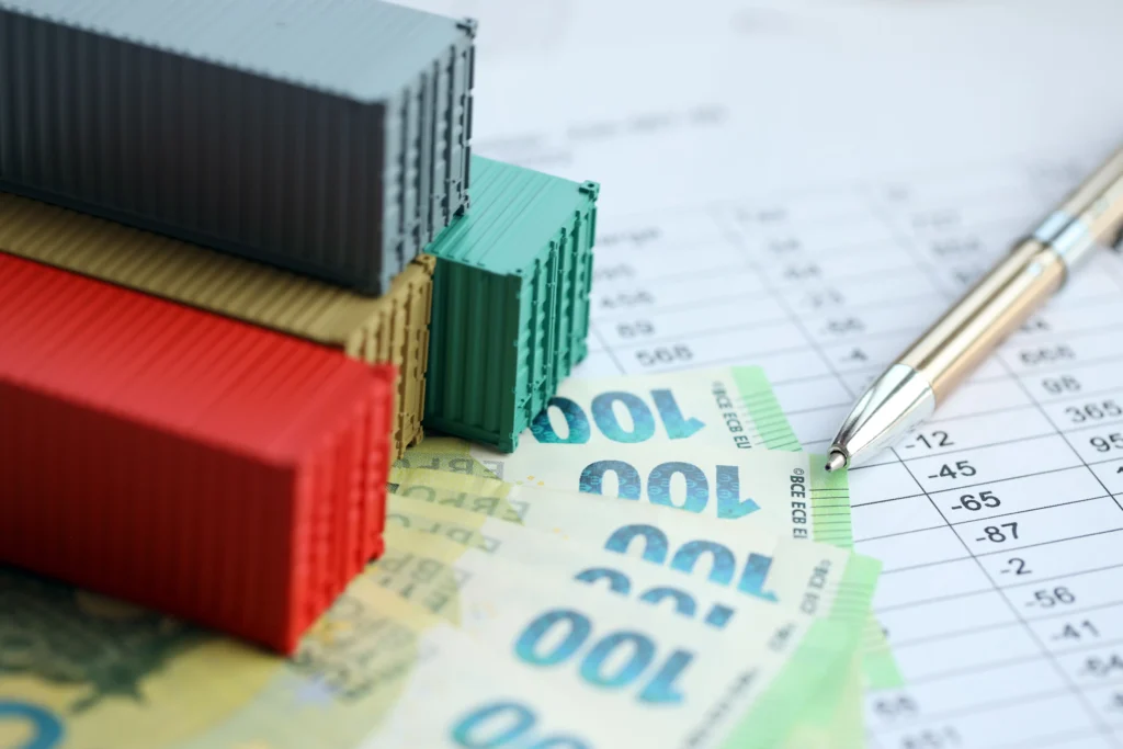 Stacked shipping containers on euro banknotes and financial data sheet representing inflation and tariff trading strategies.