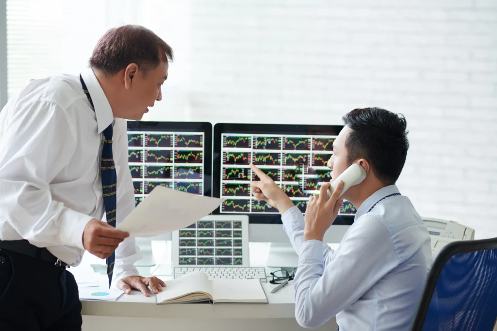 Two forex traders analyzing multiple chart screens and discussing market setups for order block mapping.