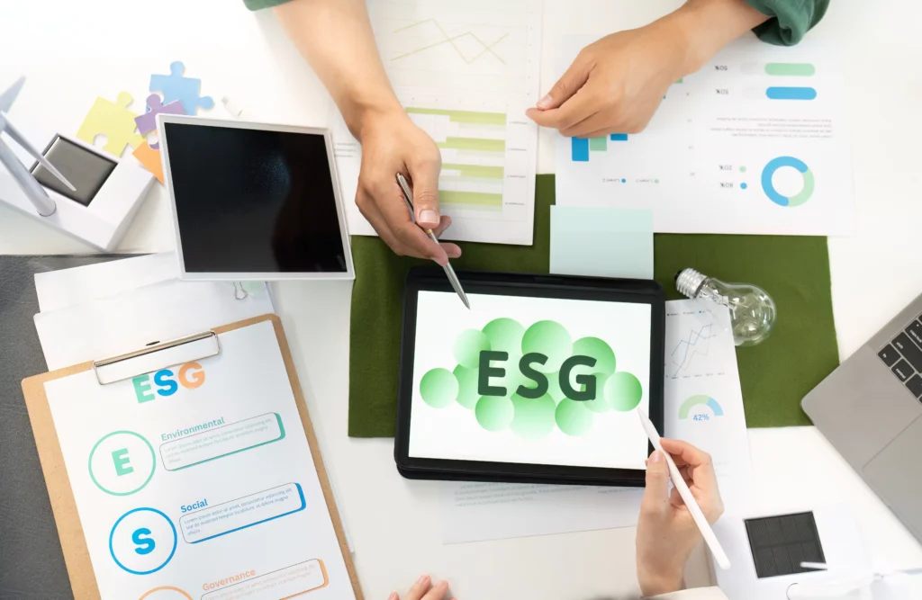 People reviewing ESG Investment Flows with charts, reports and digital tools on a desk.