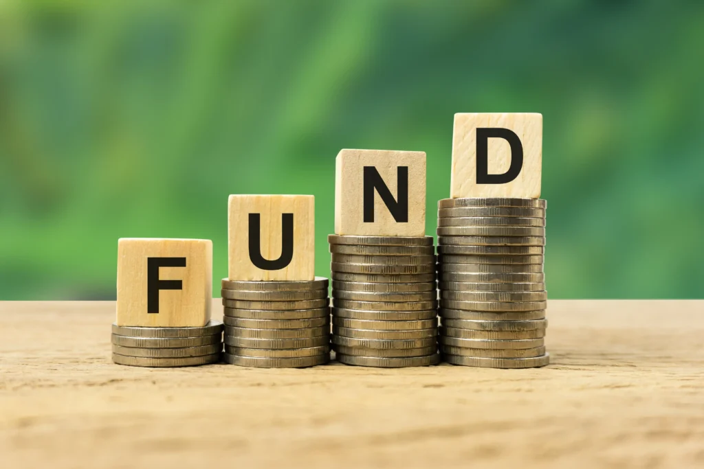 Wooden blocks spelling FUND stacked on coins, symbolizing investment growth and the concept of Fund Meaning and Types.