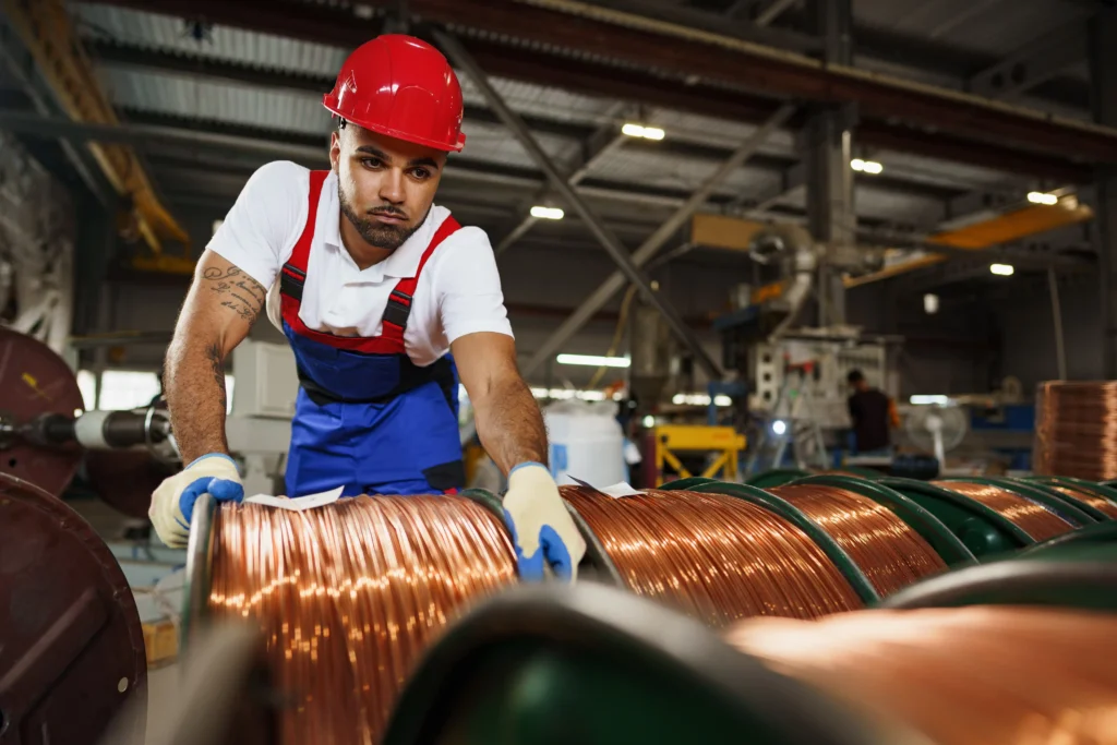 Worker handling copper wire coils inside an industrial manufacturing plant during rising global copper demand.