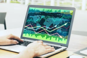 Person analyzing global forex charts on a laptop showing world map, currency trends, and market data visuals.