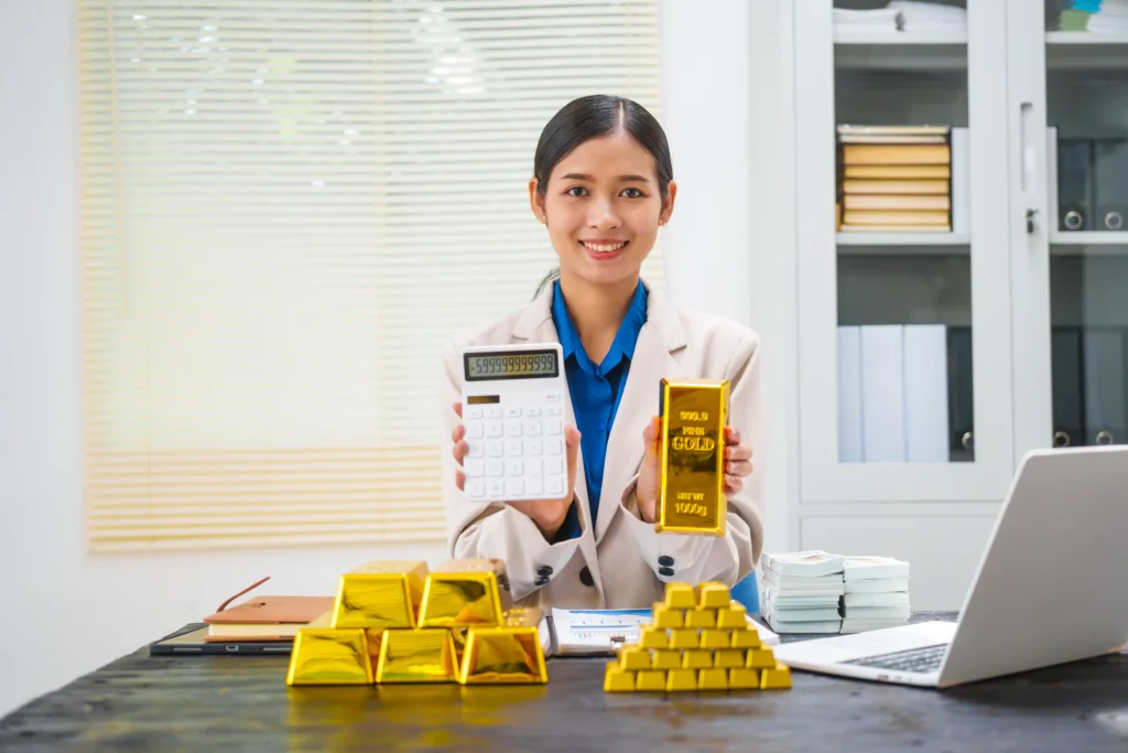 Asian businesswoman holding a calculator and a gold bar while explaining Gold Fund meaning.