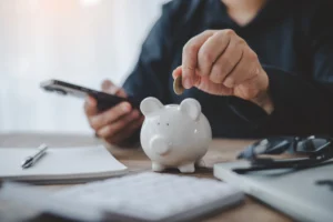 Investor saving money in a piggy bank while using a smartphone, representing smart investment and portfolio planning for 2026