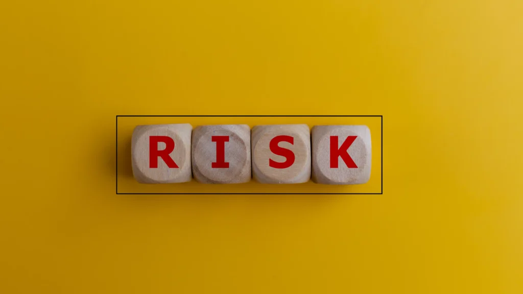 Wooden cubes spelling the word RISK on a yellow background symbolizing currency risk protection strategies.