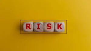 Wooden cubes spelling the word RISK on a yellow background symbolizing currency risk protection strategies.