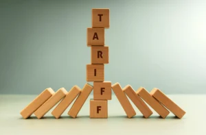 Tariff Impact on Forex illustrated with wooden blocks spelling “TARIFF” standing amid falling dominoes, symbolizing global trade volatility in 2026.