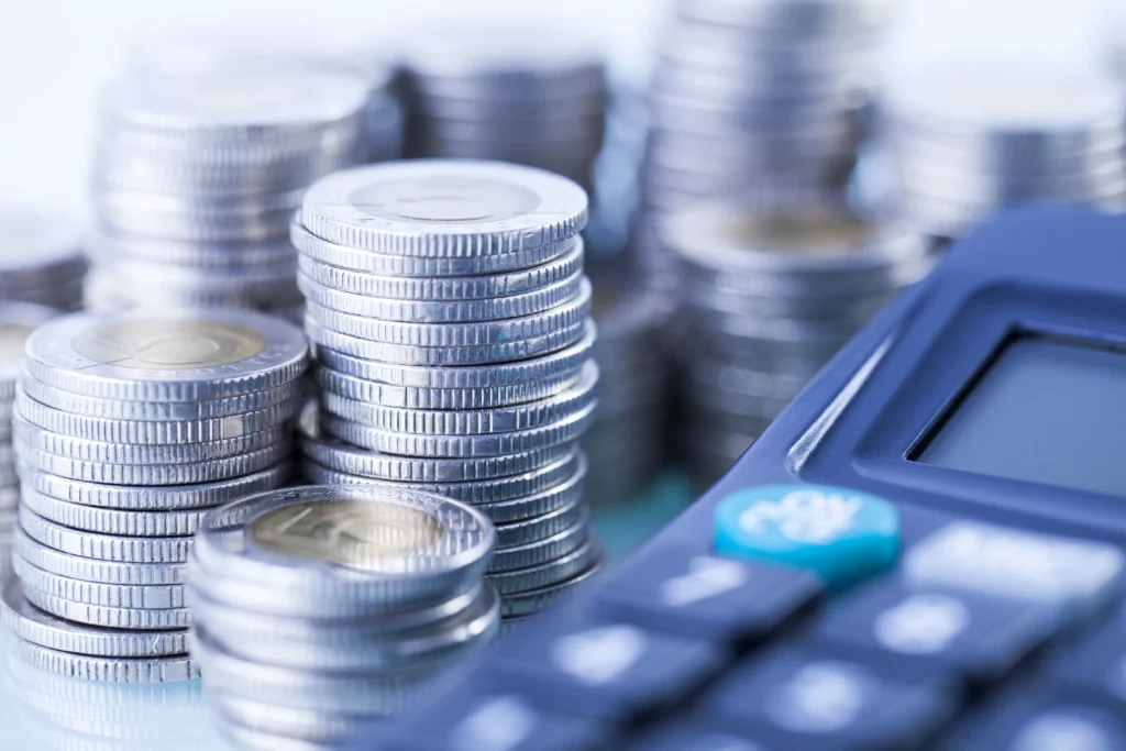 Stacks of silver coins beside a calculator representing financial comparison of Silver ETFs vs Physical Silver in 2026.