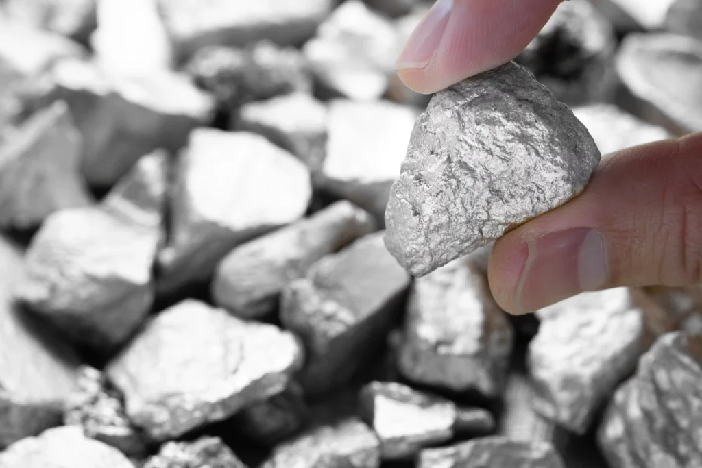 Close-up of a miner’s hand holding a raw silver ore rock, representing the early stage of the silver mining process and natural silver extraction.